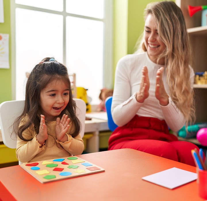 Young girl and woman clapping together at a table with a puzzle.