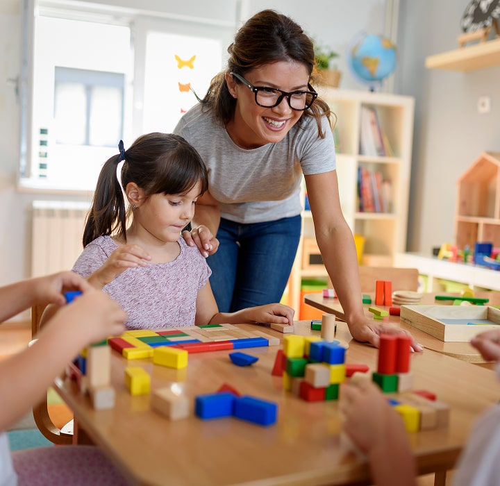 Teacher assisting a young girl with building blocks.